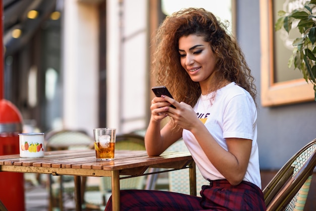 Femme arabe dans un bar urbain sur son smartphone.