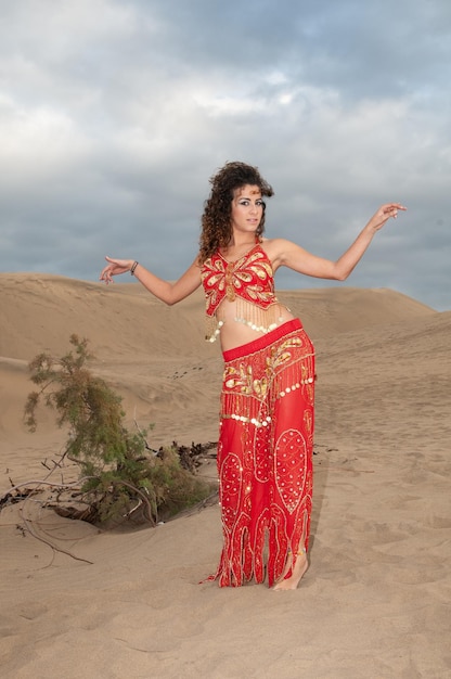 Femme arabe dansant la danse du ventre dans les dunes du désert au coucher du soleil