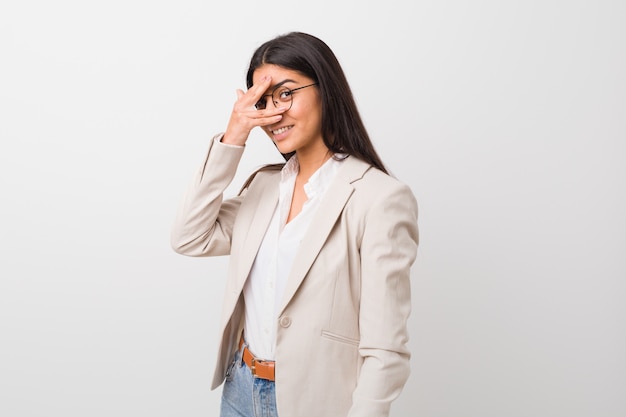 Une femme arabe de jeunes entrepreneurs isolée contre un mur blanc clignote à la caméra à travers les doigts, le visage couvrant gêné.