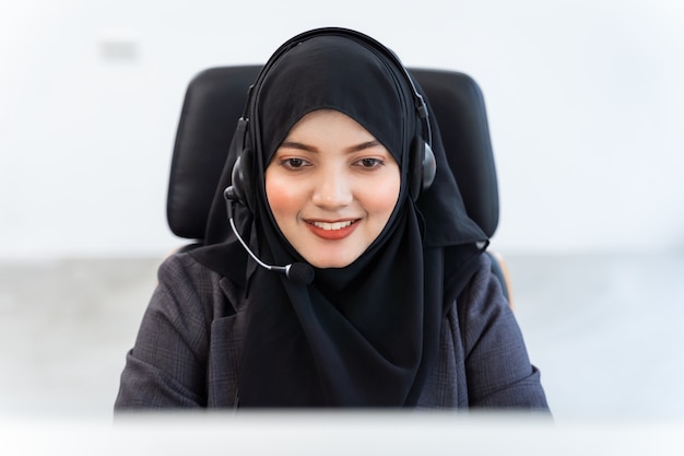 Une femme arabe ou musulmane travaille dans un opérateur de centre d'appels et un agent du service client portant des micro-casques travaillant sur ordinateur, parlant avec le client pour l'aider avec son esprit de service