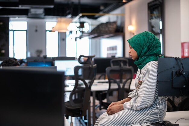 Femme arabe portant un hijab lors d'une réunion dans un brainstorming intérieur de bureau ouvert moderne, travaillant sur un ordinateur portable et un ordinateur de bureau. Mise au point sélective. Photo de haute qualité