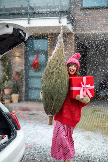 Femme avec arbre de noël enveloppé et boîte-cadeau sur le porche de sa maison