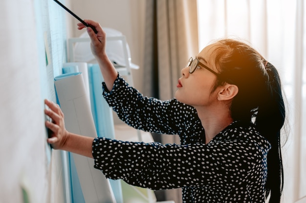 Une femme architecte décontractée et ciblée travaillant sur une planche à dessin avec un crayon à la main portant des lunettes