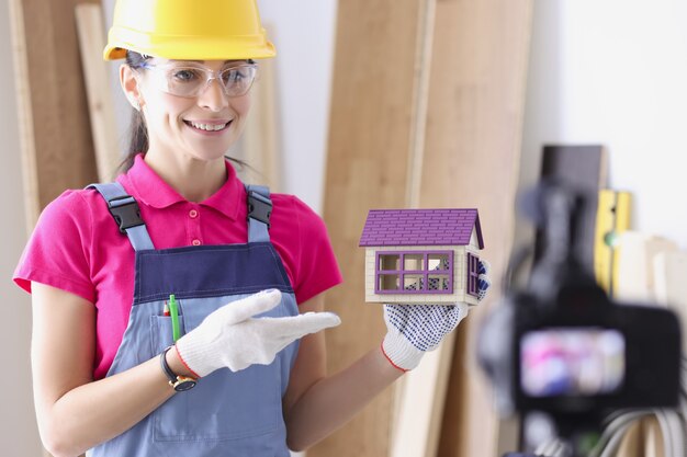 Femme architecte tenant une maison en bois jouet devant la caméra