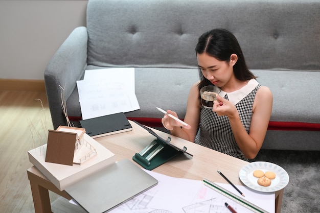 Femme architecte travaillant avec tablette informatique et plan dans le salon.