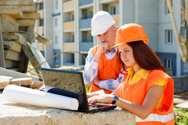 Femme architecte et travailleur de la construction à la recherche de l'ordinateur portable ensemble contre la construction