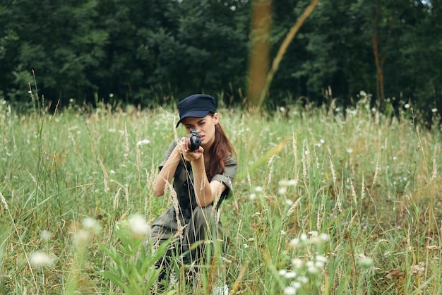 Femme avec une arme visant vers l'avant sur des squats sur des feuilles vertes en plein air