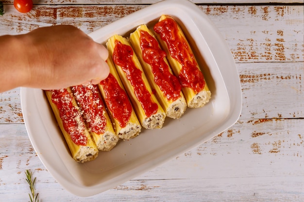 Femme arrose des pâtes cannelloni avec du fromage parmean avec de la ricotta et des champignons