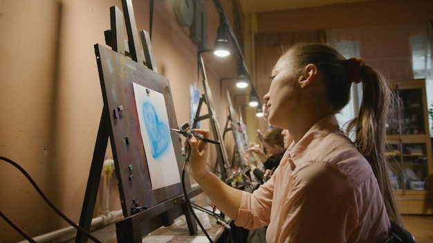 Une femme artiste apprend à peindre à l'aérographe avec du papier de teinture acrylique et un chevalet