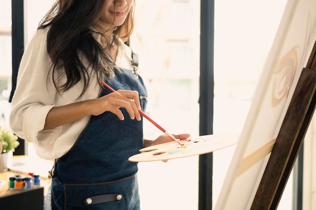 Photo femme artiste tenant un pinceau et une palette de peinture sur toile sur un lieu de travail créatif