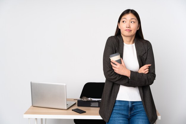 Femme asiatique d'affaires dans son lieu de travail isolé en soulevant ses épaules