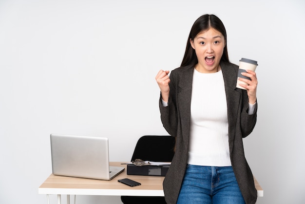 Femme asiatique d'affaires dans son lieu de travail sur le mur blanc pour célébrer une victoire en position de gagnant