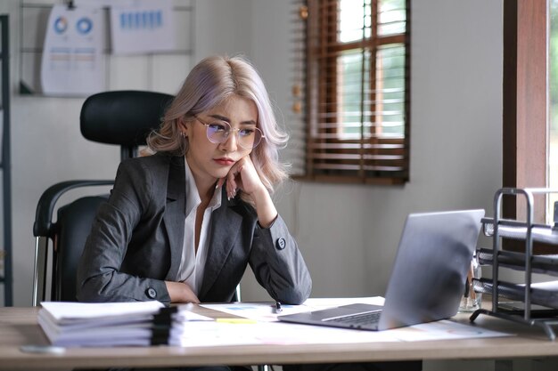 Une femme asiatique d'affaires fatiguée tient ses doigts sur ses tempes à la table de travail Journée de travail irrégulière a souligné le concept inquiet fatigué et dépassé