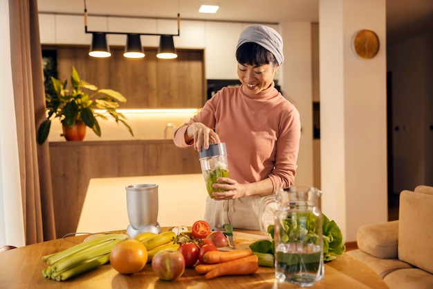 Une femme asiatique d'âge moyen heureuse prépare un smoothie frais à la maison.