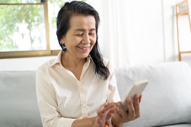 Femme asiatique d'âge moyen tenant un téléphone portable Travail à domicile souriant Belle femme asiatique mature VDO Call Conference téléphone intelligent avec concept technologique