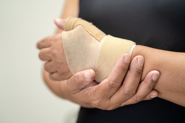 Photo une femme asiatique d'âge moyen utilise un bandage élastique pour traiter le syndrome de de quervain à la main et au doigt au bureau