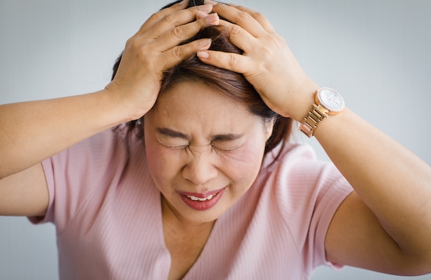 Femme asiatique âgée d'âge moyen ressentant de la douleur à cause d'un mal de tête soudain et d'une attaque cérébrale et tient sa tête avec un visage déformé et tordu. Concept de problème de cerveau et de tête.