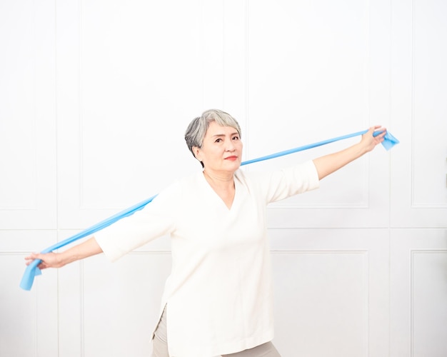 Femme asiatique âgée faisant des exercices avec une bande de résistance à la maison.