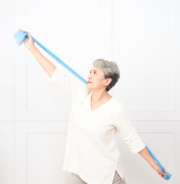 Femme asiatique âgée faisant des exercices avec une bande de résistance à la maison.