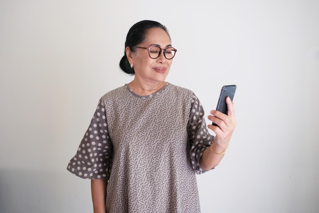 Femme asiatique âgée souriant tout en regardant son téléphone portable