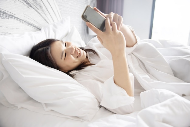Photo femme asiatique à l'aide de médias sociaux sur téléphone portable en position couchée dans son lit le matin