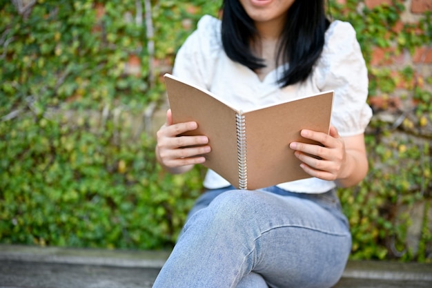 Une femme asiatique aime lire un livre ou un roman dans son beau jardin ou son arrière-cour