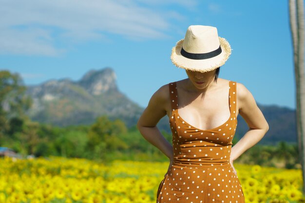 Femme asiatique des années 40 LGBT transgenre express sentiment heureux sourire amusant sous le soleil dans le champ de fleurs jaunes de tournesol sur la montagne de ciel bleu Femme pose pour la prise de vue de mode dans le paysage extérieur