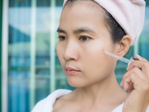 femme asiatique appliquer le sérum cosmétique sur son visage.