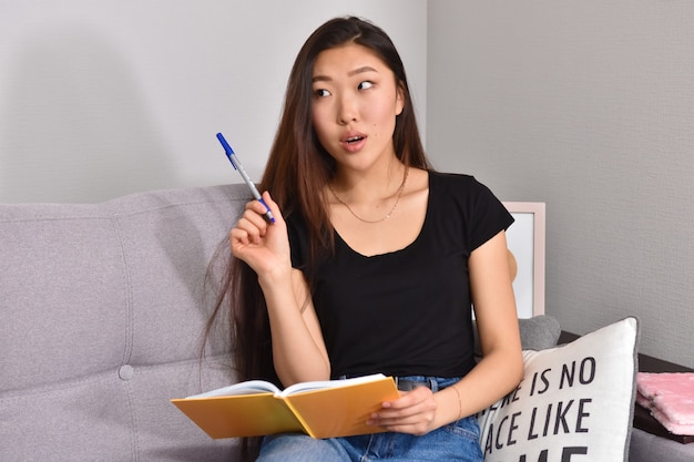 Femme asiatique assise sur un canapé et un cahier orange