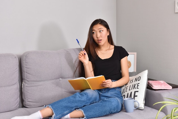 Femme asiatique assise sur un canapé et un cahier orange