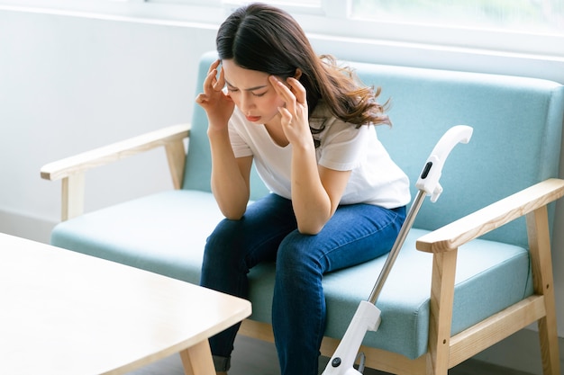 Femme asiatique assise sur une chaise avec une expression fatiguée lors du nettoyage de la maison