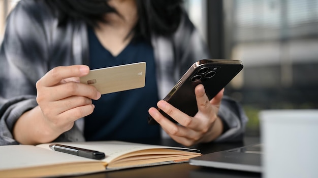 Une femme asiatique assise dans le café tenant une carte de crédit et son smartphone