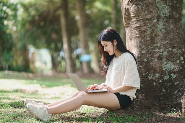 Femme asiatique assise sur un pique-nique et une pelouse au parc travaillant sur un ordinateur portable