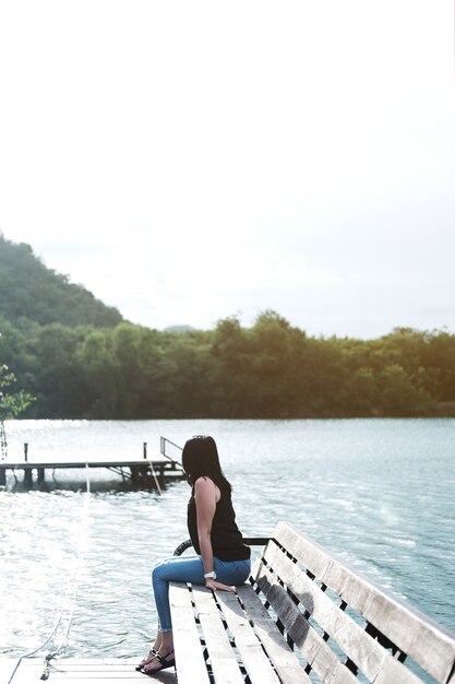 Femme asiatique assise seule sur un banc en bois près du lac.