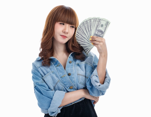 Femme asiatique aux cheveux bruns tenant et se sentant heureuse avec des billets de banque américains qui s'étalaient dans sa main, elle souriante, prise de vue en studio sur fond blanc.