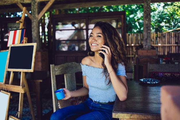 Femme asiatique ayant une conversation au téléphone tenant une tasse à la main assise à l'extérieur
