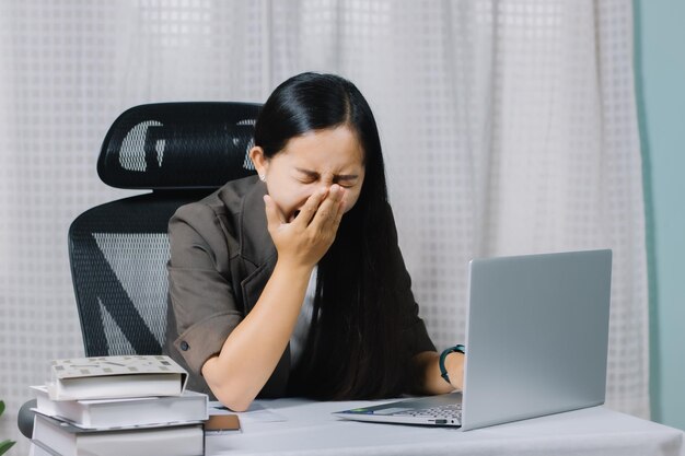 Femme asiatique bâillant tout en travaillant sur un ordinateur portable dans son bureau.