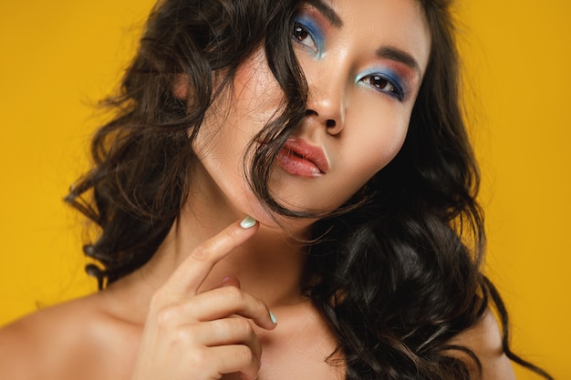 Femme asiatique avec de beaux cheveux bouclés et maquillage sur jaune