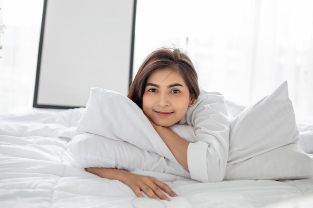 Femme asiatique Belle jeune femme souriante assise et dormant dans un lit blanc et s'étirant le matin dans la chambre après s'être réveillée dans son lit complètement reposée