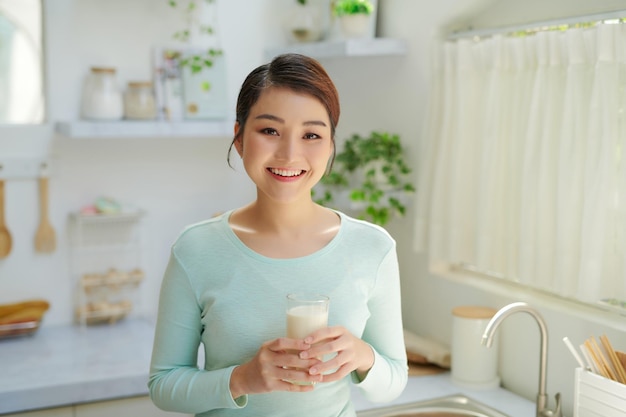 Une femme asiatique boit du lait dans la cuisine