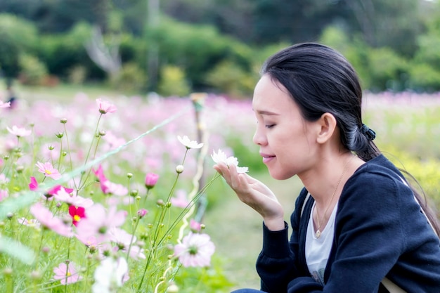 Photo femme asiatique de bonheur toucher et sentir fleur de cosmos dans le parc