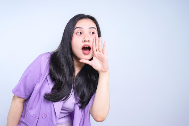 Une femme asiatique avec la bouche ouverte lève les mains et crie une annonce.