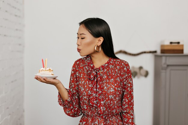 Une femme asiatique brune souffle des bougies sur un gâteau d'anniversaire