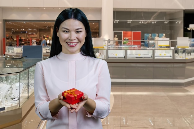 Femme asiatique brune souriante vous donnant une boîte-cadeau rouge avec les deux mains