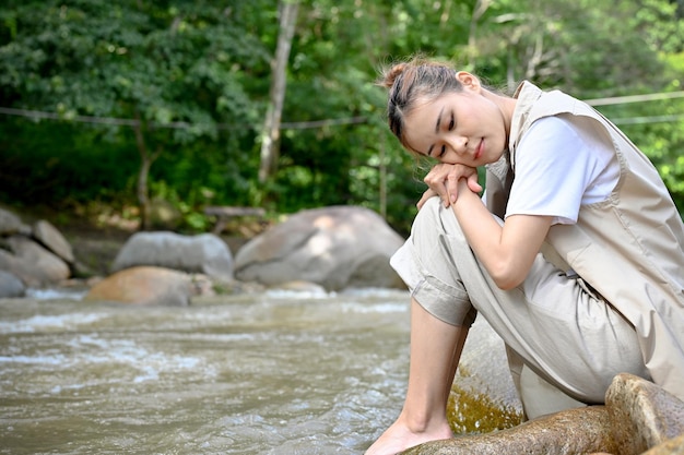 Femme asiatique calme et détendue assise sur le rocher près de la rivière dans la belle forêt