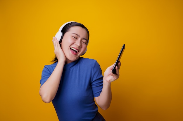 Femme asiatique avec un casque d'écoute de la musique depuis un téléphone intelligent sur jaune.