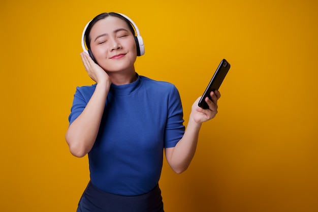 Femme asiatique avec un casque d'écoute de la musique depuis un téléphone intelligent sur jaune.