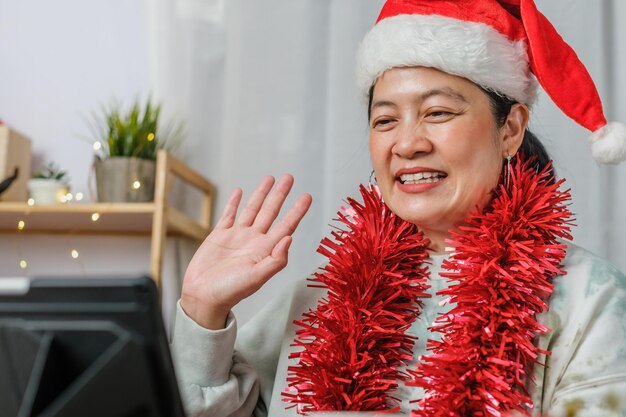 Une femme asiatique célèbre le nouvel an et la fête de noël avec des amis d'appel vidéo sur tablette à la maison