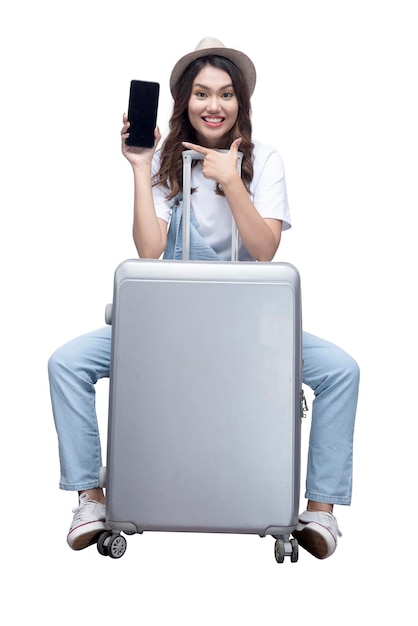 Femme asiatique avec un chapeau assis sur une valise et montrant un écran de téléphone portable vide