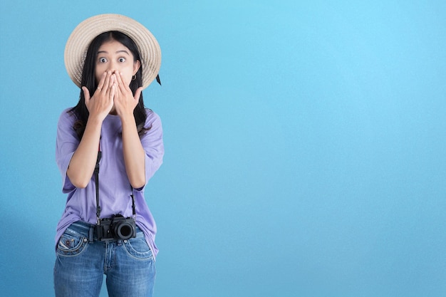 Femme asiatique avec chapeau et caméra debout avec une expression choquée avec un fond coloré